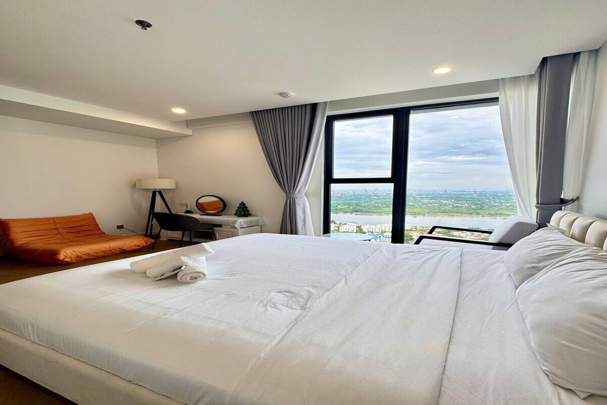 A hotel room with a large bed, a desk, a chair, and a view of the city.