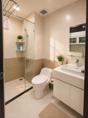 A modern bathroom with a glass-enclosed shower, a toilet, a sink with a mirror, and a small potted plant. - The Sun Avenue - Lalaland & Chill Sky Pool (Ho Chi Minh City)