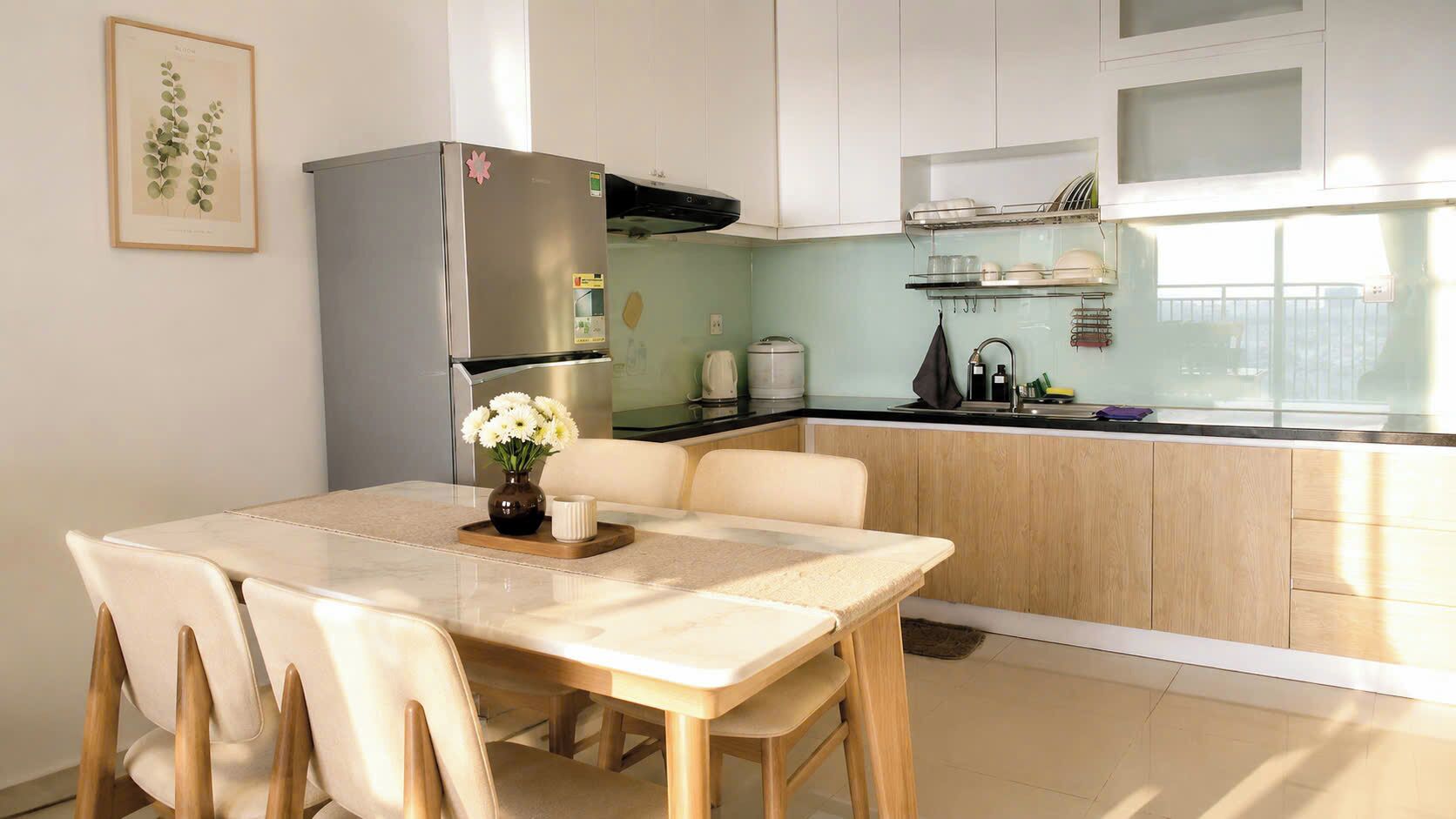 Eine moderne Küche mit Kühlschrank, Esstisch, Stühlen und einem Blumenstrauß.