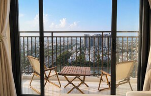 Ein Balkon mit Holztisch und zwei Stühlen, mit Blick auf eine Stadtlandschaft mit Gebäuden und Grünflächen.