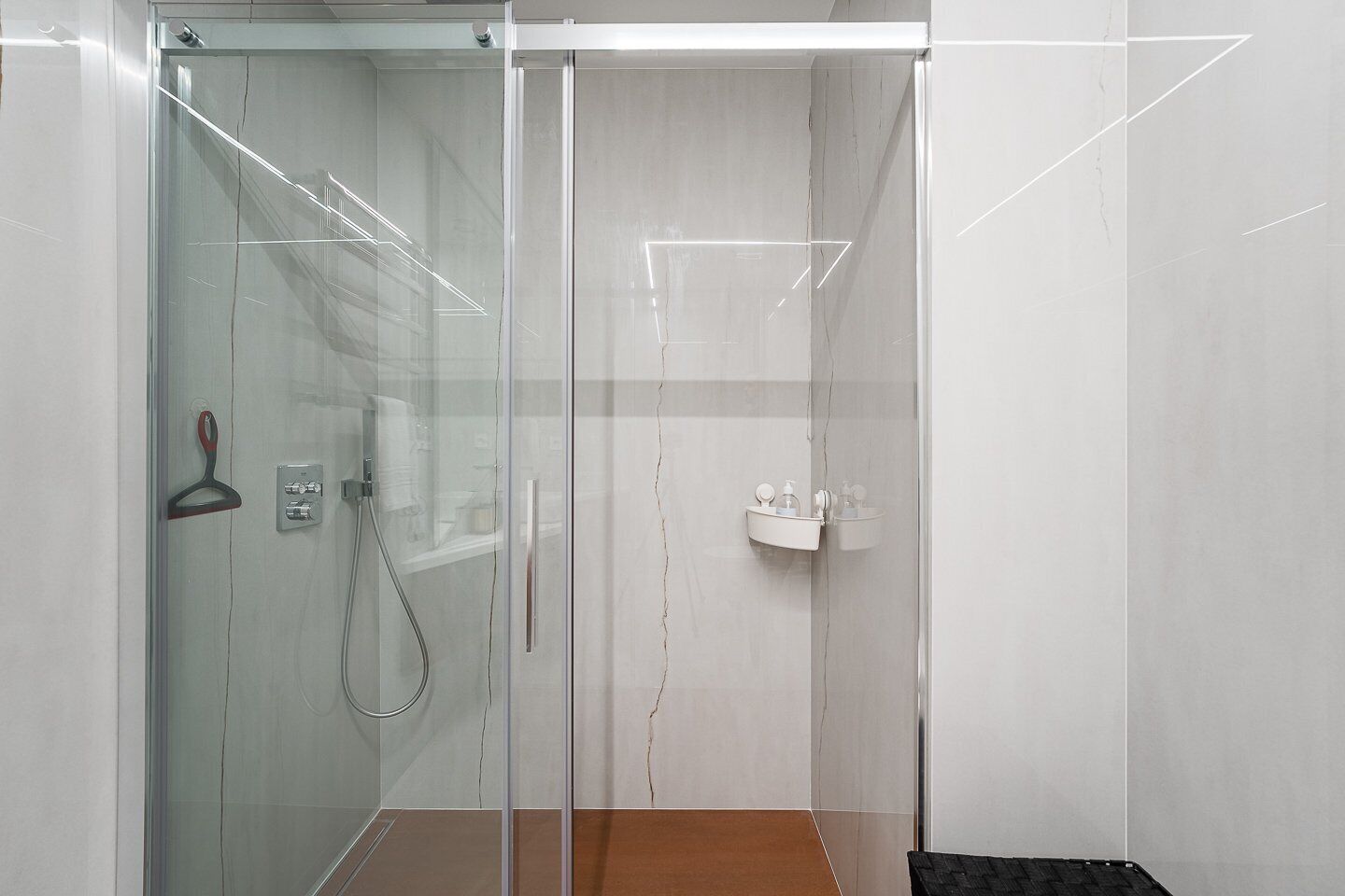 Une cabine de douche moderne dotée d’une porte en verre, d’un pommeau de douche à main et d’un lavabo fixé au mur.