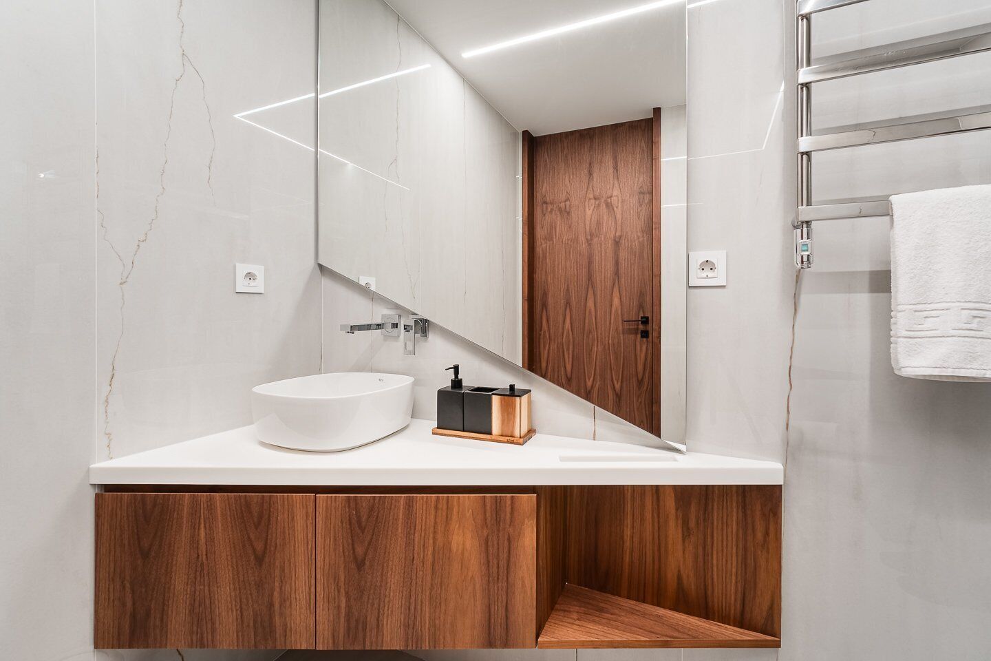 Un bagno moderno con un lavandino in marmo bianco, mobiletti in legno e un grande specchio.