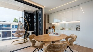 Een moderne eethoek met een ronde houten tafel, rieten stoelen en een hangstoel.