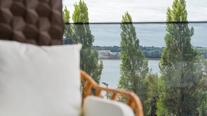 Uitzicht vanuit een raam op een wateroppervlak met hoge bomen en een verre kustlijn.