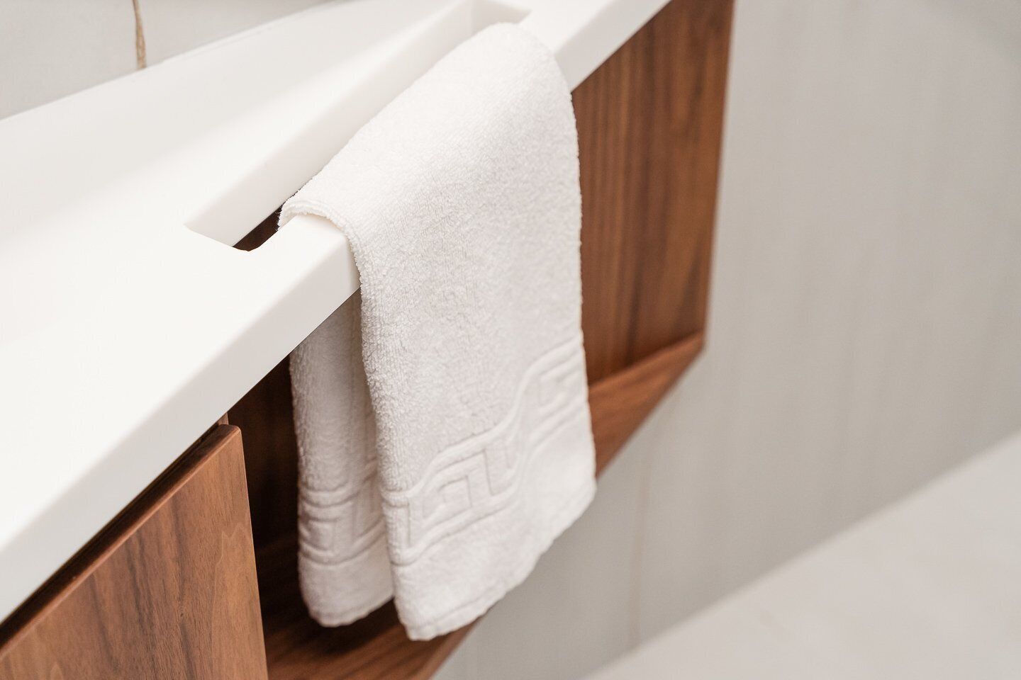 A white towel hanging on a wooden towel rack in a bathroom.