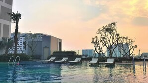 A swimming pool with lounge chairs, a palm tree, and modern buildings in the background. - Century Diamond Alnata Plus - Tan Phu (Ho Chi Minh City)