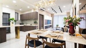A modern kitchen with a dining area, featuring a chandelier, wooden cabinets, and a dining table set for four. - Century Diamond Alnata Plus - Tan Phu (Ho Chi Minh City)