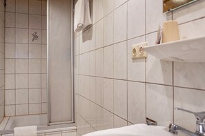 Un baño con ducha, lavamanos y estante con artículos de aseo.