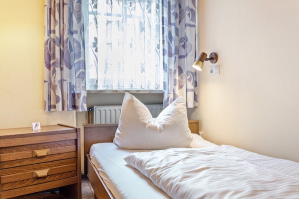 Un dormitorio con cama, cómoda de madera, radiador y ventana con cortinas.