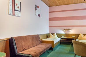 A room with a brown sofa, a single bed, a small table, and a chair.