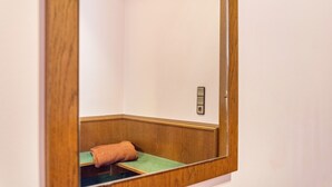 Un coin de pièce avec un banc en bois, un coussin vert et un interrupteur fixé au mur.