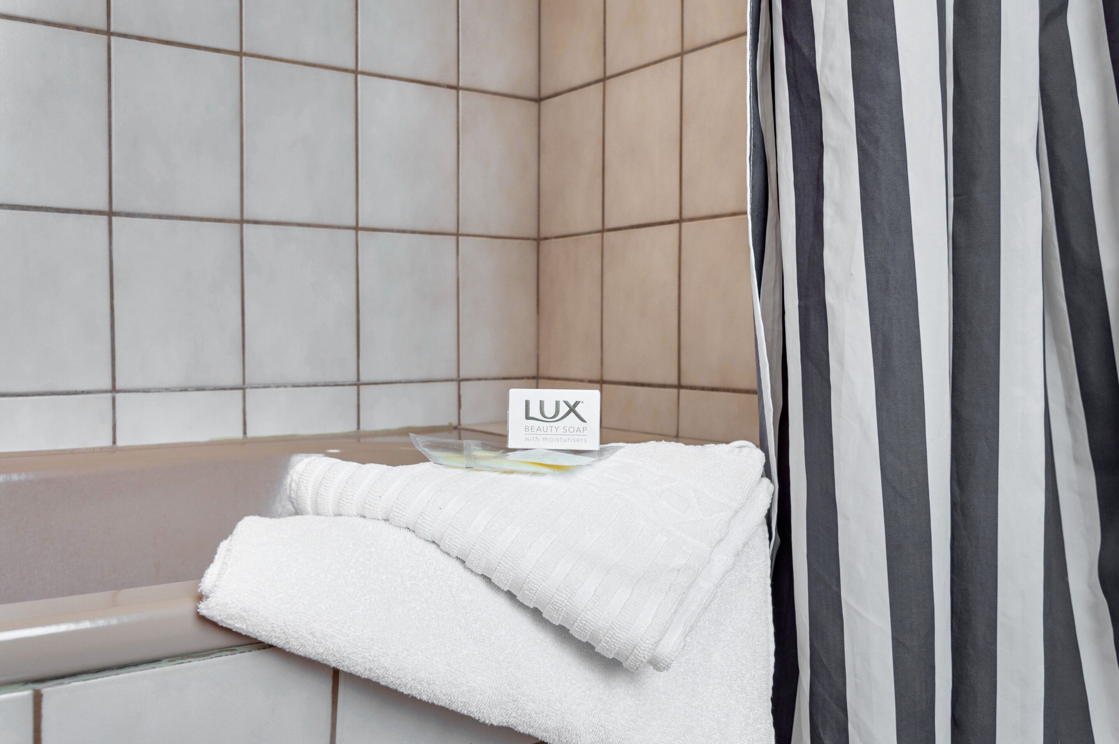 Un baño con bañera, una toalla y un cartel que dice 'LUX BEAUTY SOAP con hidratantes'.
