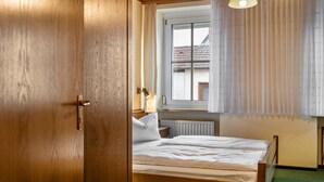 A bedroom with a wooden door, a bed with white bedding, a window with curtains, and a radiator. - Room 2 - Double room with Wi-Fi (Lehrberg)