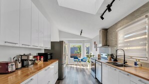 A modern kitchen with white cabinets, a wooden countertop, and a view to the outside.