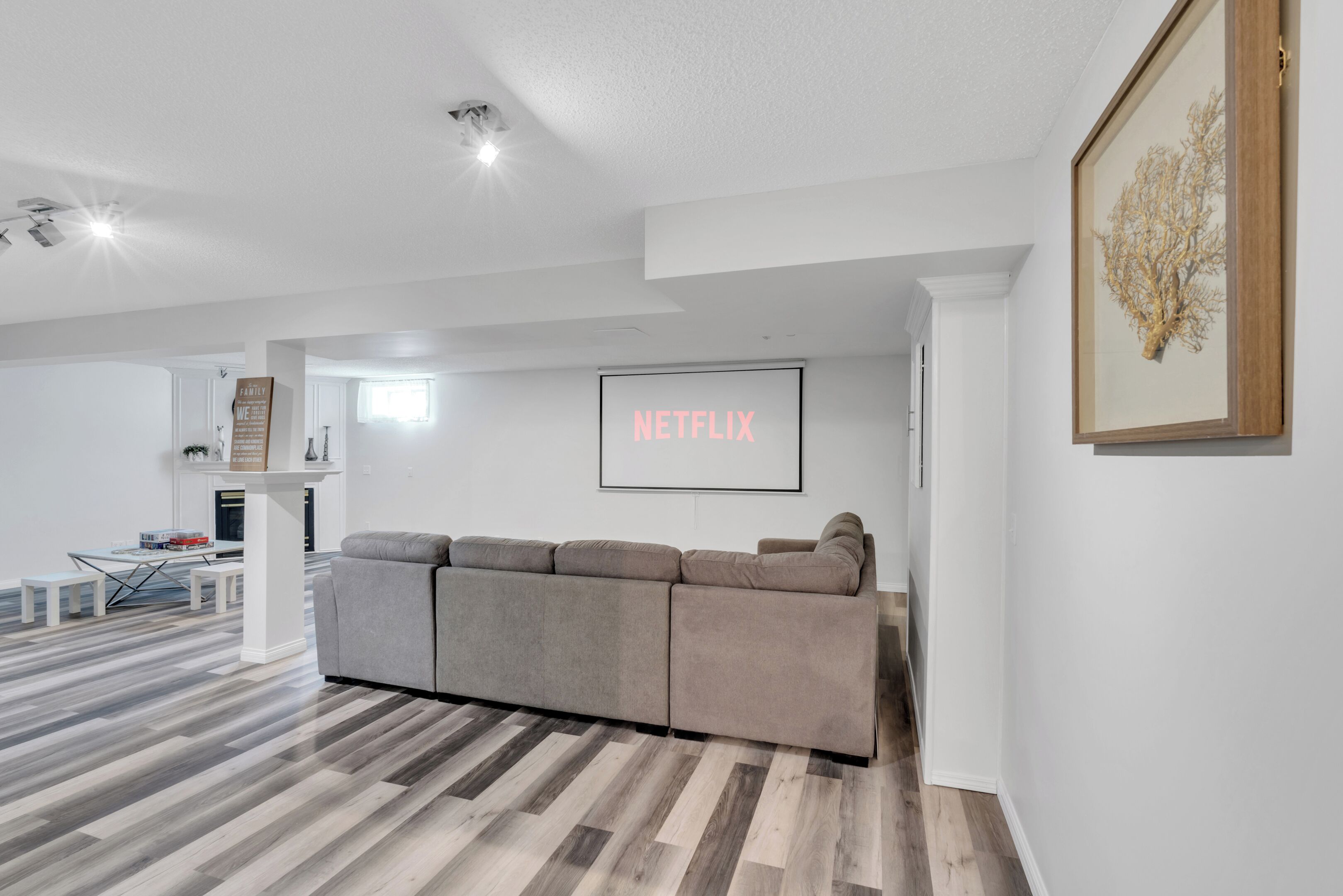 Uma sala de estar moderna com um sofá seccional, uma TV de tela plana na parede e piso de madeira.