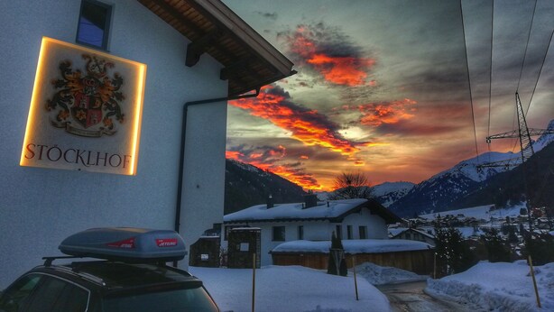 A building with a coat of arms sign, a car parked in front, and a snowy landscape with mountains in the background.