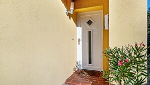 Una casa de fachada color crema, techo rojo, puerta blanca con una ventana en forma de diamante y un pequeño escalón de ladrillo que lleva a la puerta.