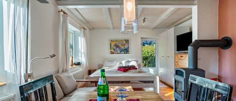 A cozy room with a bed, a table with a bottle and glasses, a wooden ceiling, and a fireplace.