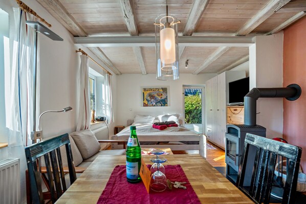 A cozy room with a bed, a table with a bottle and glasses, a wooden ceiling, and a fireplace.