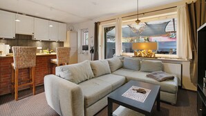 A living room with a sofa, a coffee table, and a dining area with chairs and a kitchen in the background.