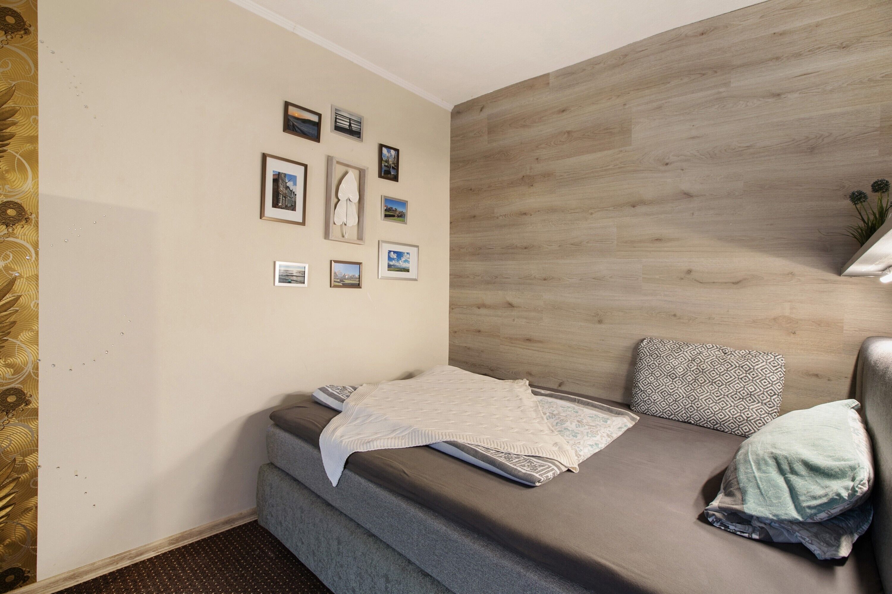 Een kleine kamer met een bed, een muur met ingelijste foto's en een houten accentmuur.