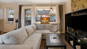 A living room with a sofa, a coffee table, a TV, and a window with curtains.