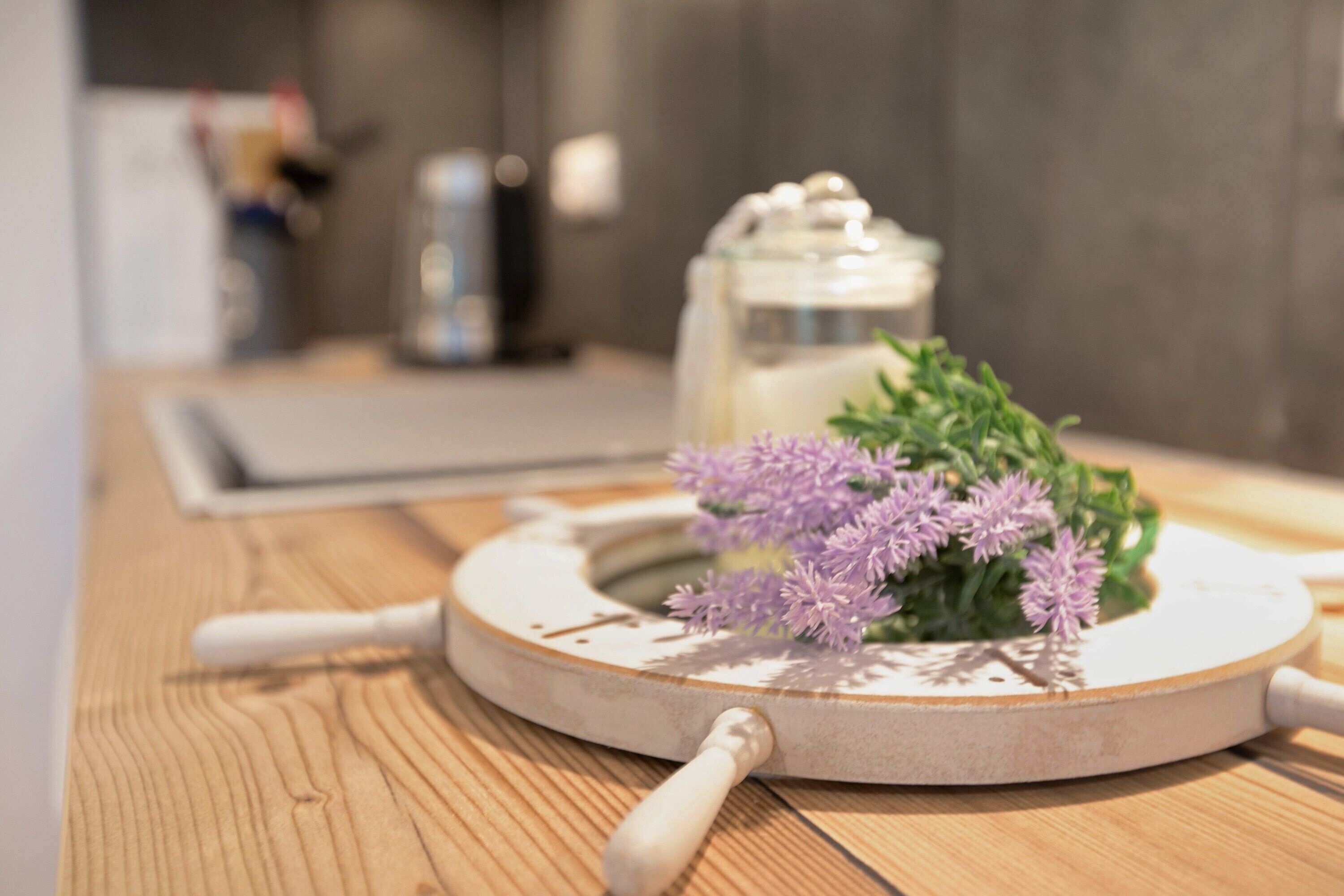 A wooden surface with a white circular object, a jar, and purple flowers.