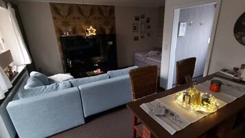A living room with a sofa, a TV, a dining table with a placemat, and a decorative light.
