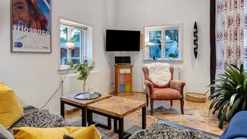 Un salon avec un canapé, un fauteuil, une table basse, un téléviseur et une affiche accrochée au mur.