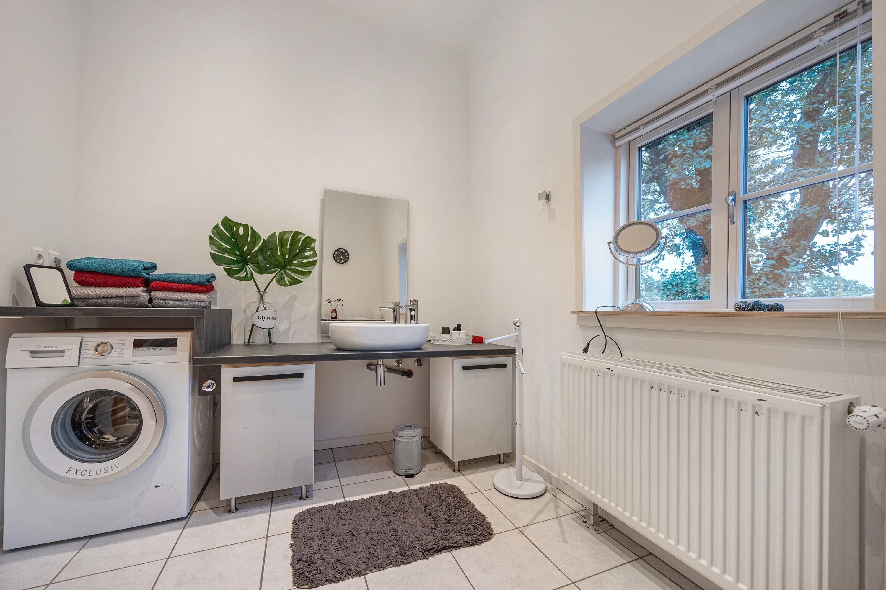 Un baño moderno con lavadora, lavamanos y ventana con vista a árboles.