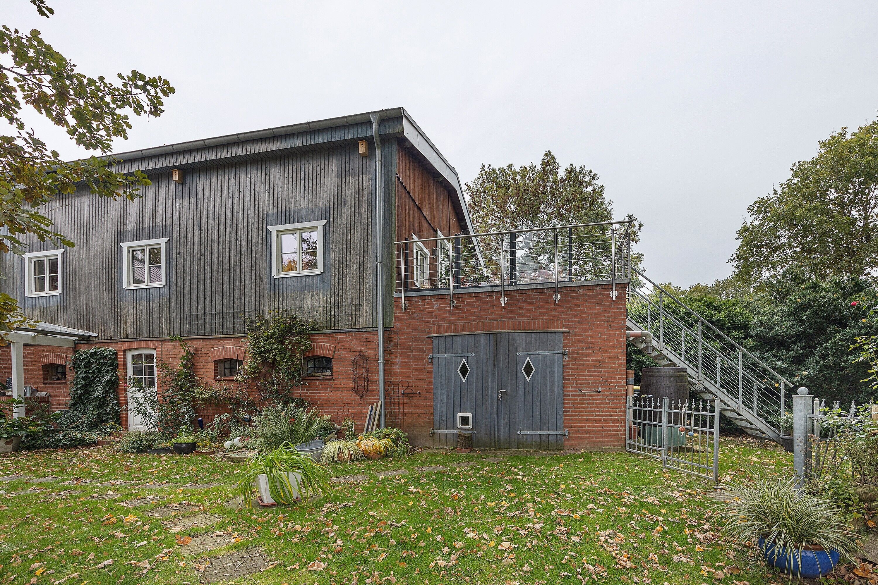 A two-story building with a brick facade, a metal staircase, and a small garden area with potted plants.