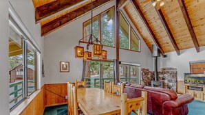 Amplia habitación con una mesa de comedor de madera, sofá de cuero rojo y ventanas grandes con vistas al exterior.