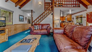 Amplia sala de estar con techo de madera, un sofá de cuero marrón grande, una mesa de centro de madera y una escalera que lleva a un nivel superior.