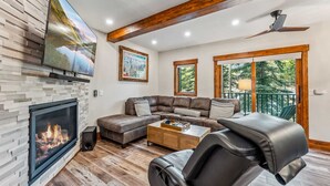 A modern living room with a fireplace, a sectional sofa, a coffee table, and a television mounted on the wall. - Breck Ski-in Retreat – Walk to Gondola & Lifts (Breckenridge)