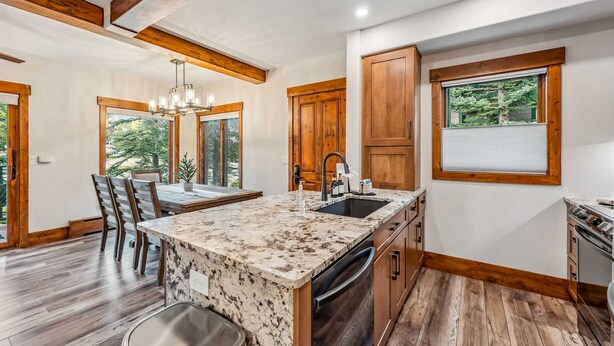 A modern kitchen with a granite countertop, wooden cabinetry, and a built-in dishwasher. - Breck Ski-in Retreat – Walk to Gondola & Lifts (Breckenridge)