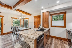 A modern kitchen with a granite countertop, wooden cabinetry, and a built-in dishwasher. - Breck Ski-in Retreat – Walk to Gondola & Lifts (Breckenridge)