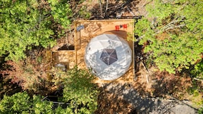 Une structure sphérique ornée d’un motif géométrique, entourée d’une terrasse en bois et de chaises rouges, située dans une zone boisée.
