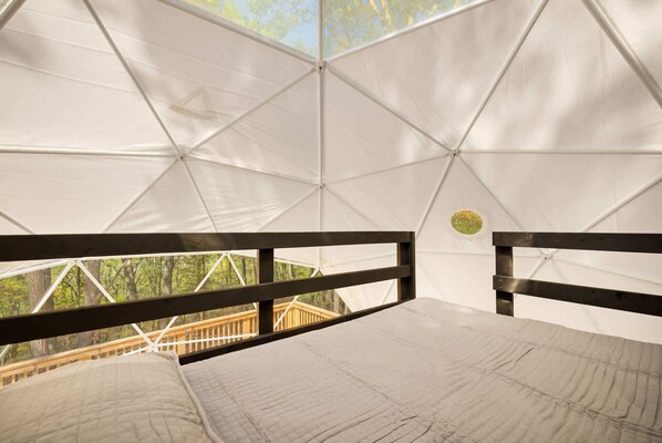 A tented accommodation with a bed, wooden railings, and a view of a forested area.