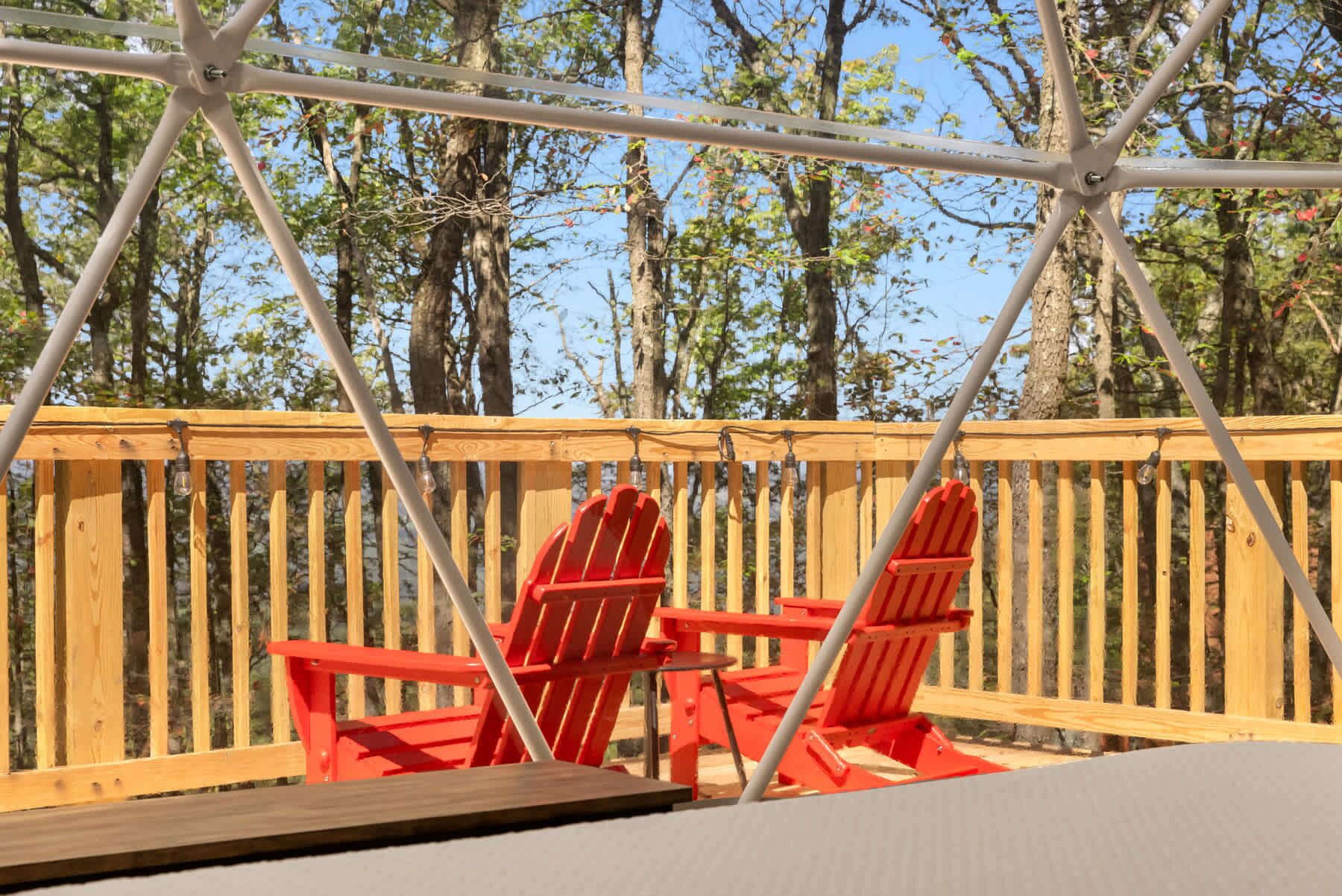 Une terrasse en bois avec deux chaises Adirondack rouges et une rambarde en métal.
