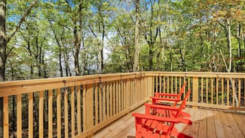 A wooden deck with a railing, two red Adirondack chairs, and a forested backdrop.
