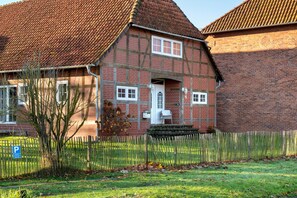 Une maison traditionnelle à colombages, avec un toit recouvert de tuiles rouges, une porte blanche et un petit porche.