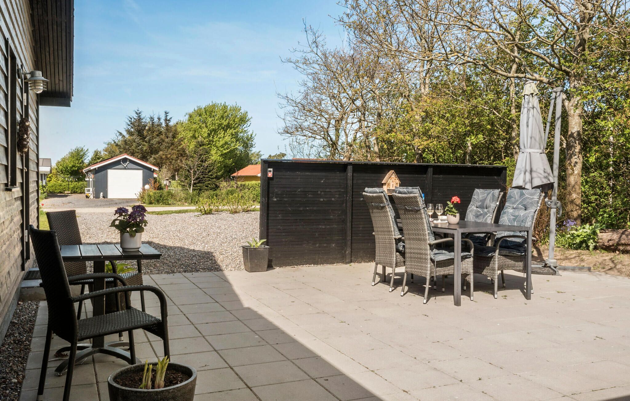 A patio area with outdoor furniture, a table, and chairs. There is a small garden with plants and a potted plant on the table.
