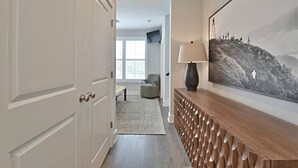 A hallway with a white door, a wooden console table with a lamp, and a large black and white photograph on the wall.