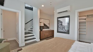 A bedroom with a bed, a staircase, a wardrobe, and a wall-mounted air conditioner.
