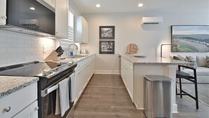 A modern kitchen with white cabinetry, a granite countertop, and a stainless steel range hood. There is a small island with a sink and a chair, and a large window with a view of a landscape.