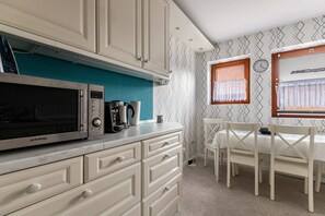 A kitchen with a microwave, coffee maker, and cabinets. There is a dining table with chairs and a window with blinds. - Apartment 'Davio' with Private Terrace, Private Garden and Wi-Fi (Lohe-Rickelshof)