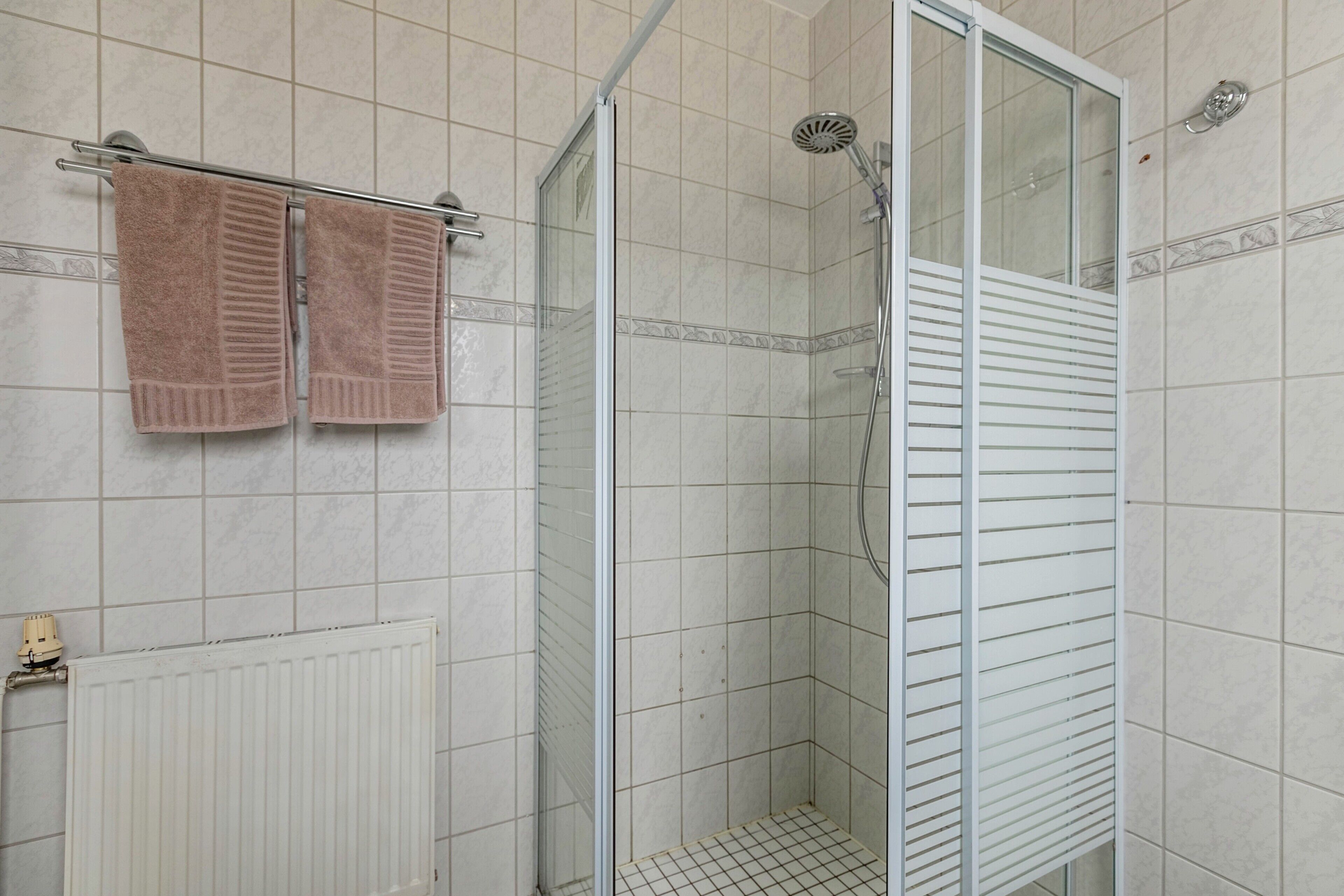 A bathroom with a shower, a towel rack with two towels, and a radiator.