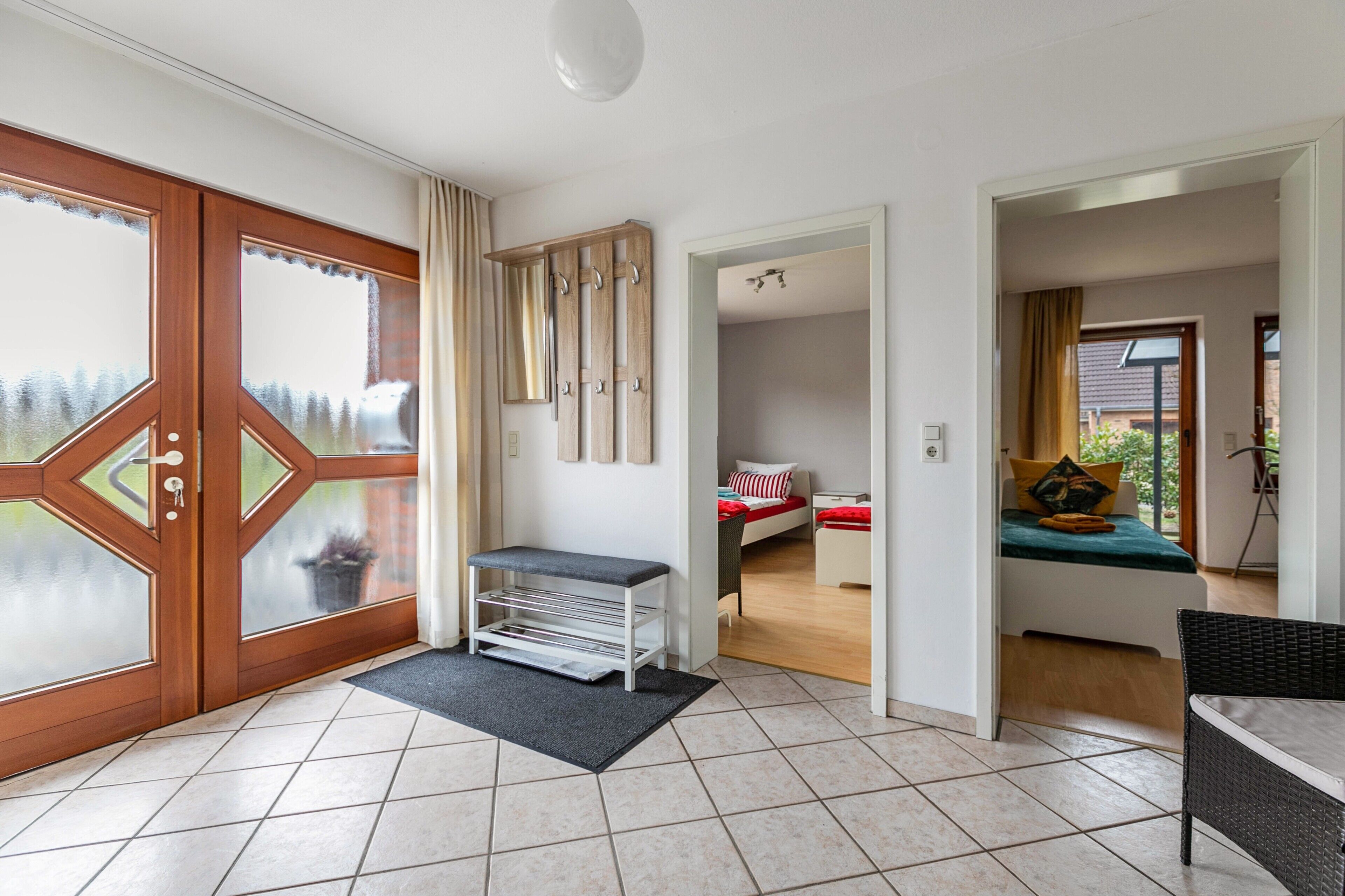 Quarto de hotel com porta de madeira, um banco, cama com roupa de cama vermelha e branca e vista pela janela.