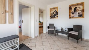 A living room with a bench, two wicker chairs, a small table, and two paintings on the wall.