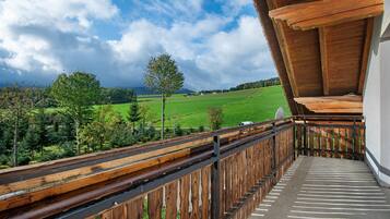 Un balcon doté d’une balustrade en bois, d’où l’on peut admirer un paysage verdoyant et un ciel nuageux.